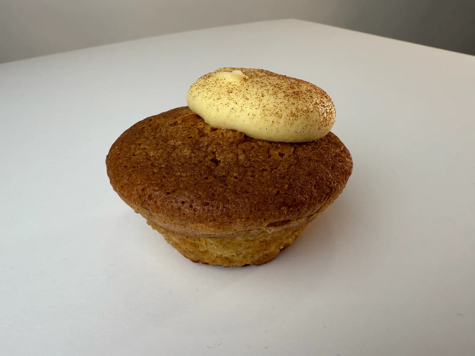 The same bun from the side under flat kitchen light, the cream sitting to one side, the paper case gone