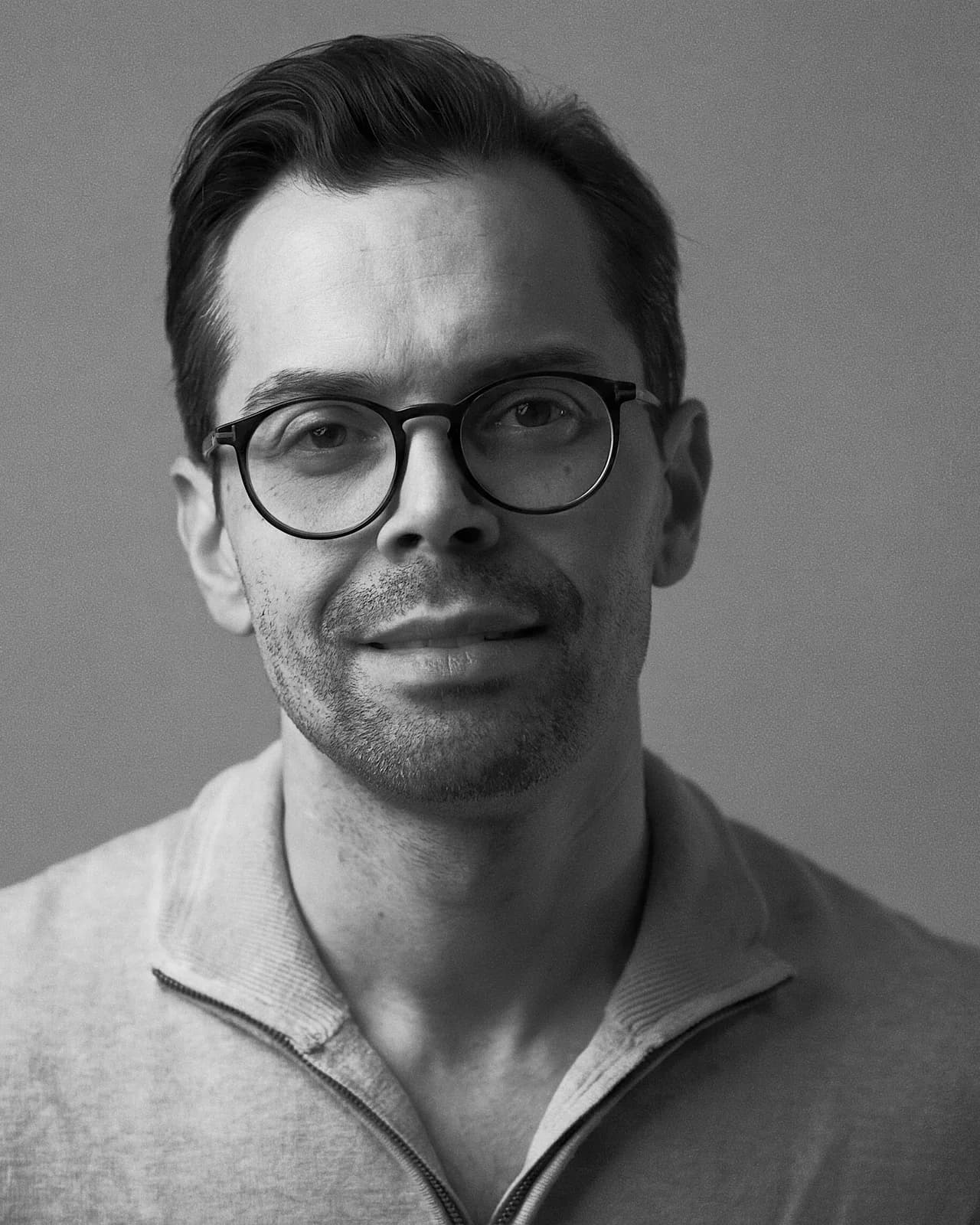 Rune Johannessen, photographed in a studio against a warm grey backdrop, wearing glasses and a light knitted top